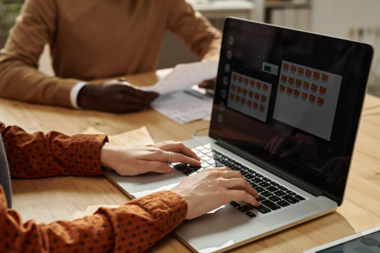 Close-up of businesswoman typing on laptop while sitting at table with colleagues at meeting