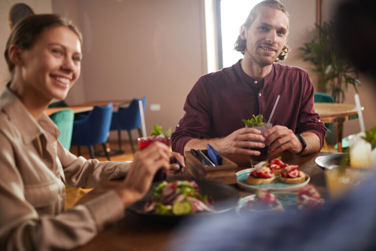 Group of friends enjoying lunch together sitting at table in cafe, focus on handsome young man, copy space