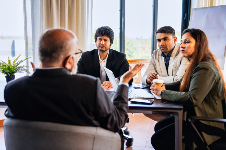 Indian Asian group of four successful business professionals in formal attire having a meeting and discussing strategies in a conference room across a table