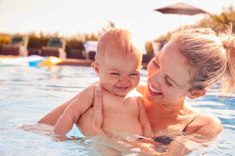 Mother With Baby Daughter Having Fun On Summer Vacation Splashing In Outdoor Swimming Pool