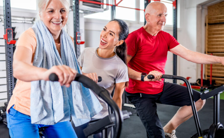 Senior couple biking at the gym with personal trainer