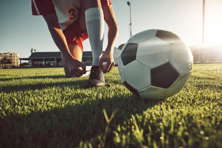Soccer, ball and tying shoes for sports day of player on the grassy field for match, game or compet.